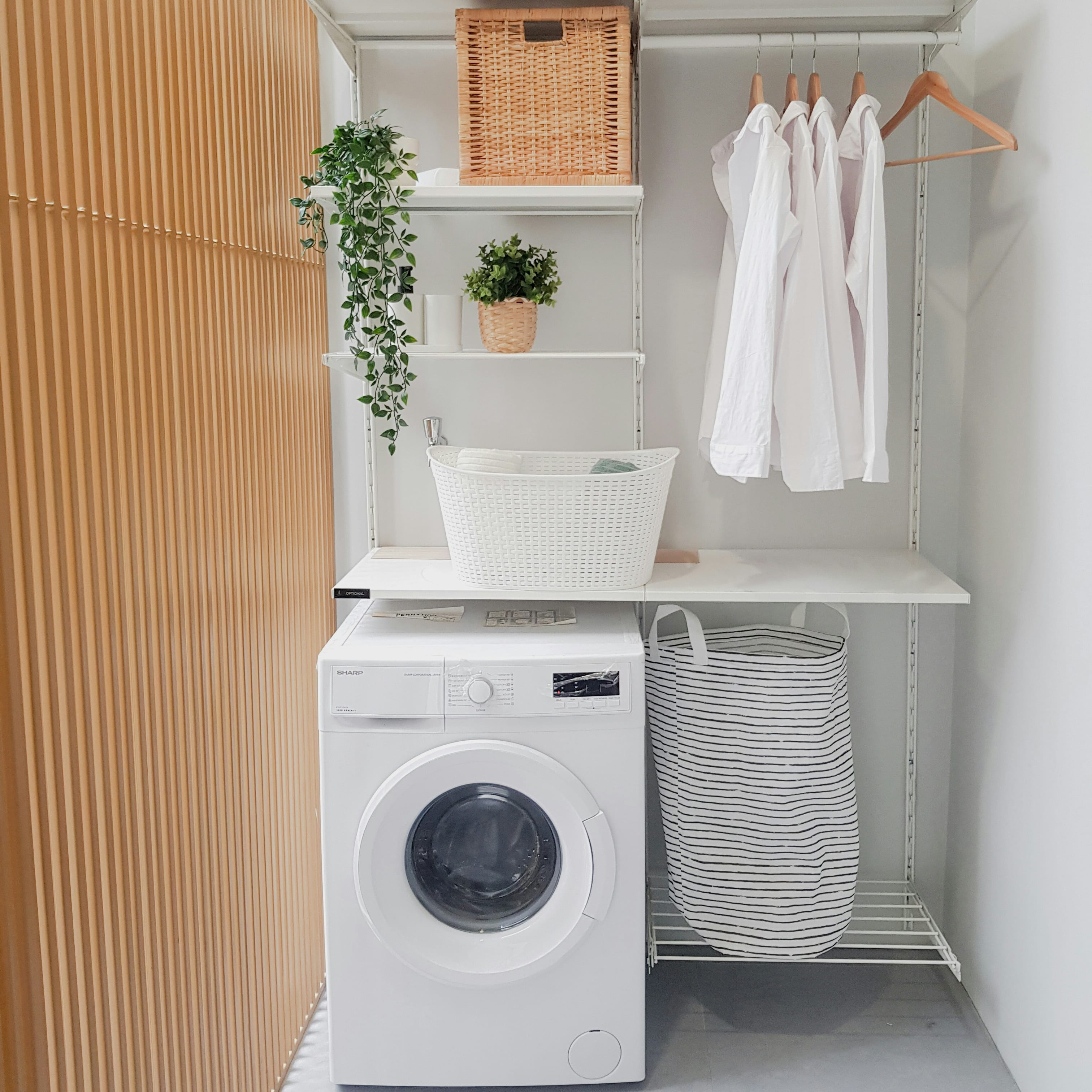 comment aménager une buanderie – Un coin buanderie avec une machine à laver, un panier à linge et des étagères isolé par une claustra en bois.