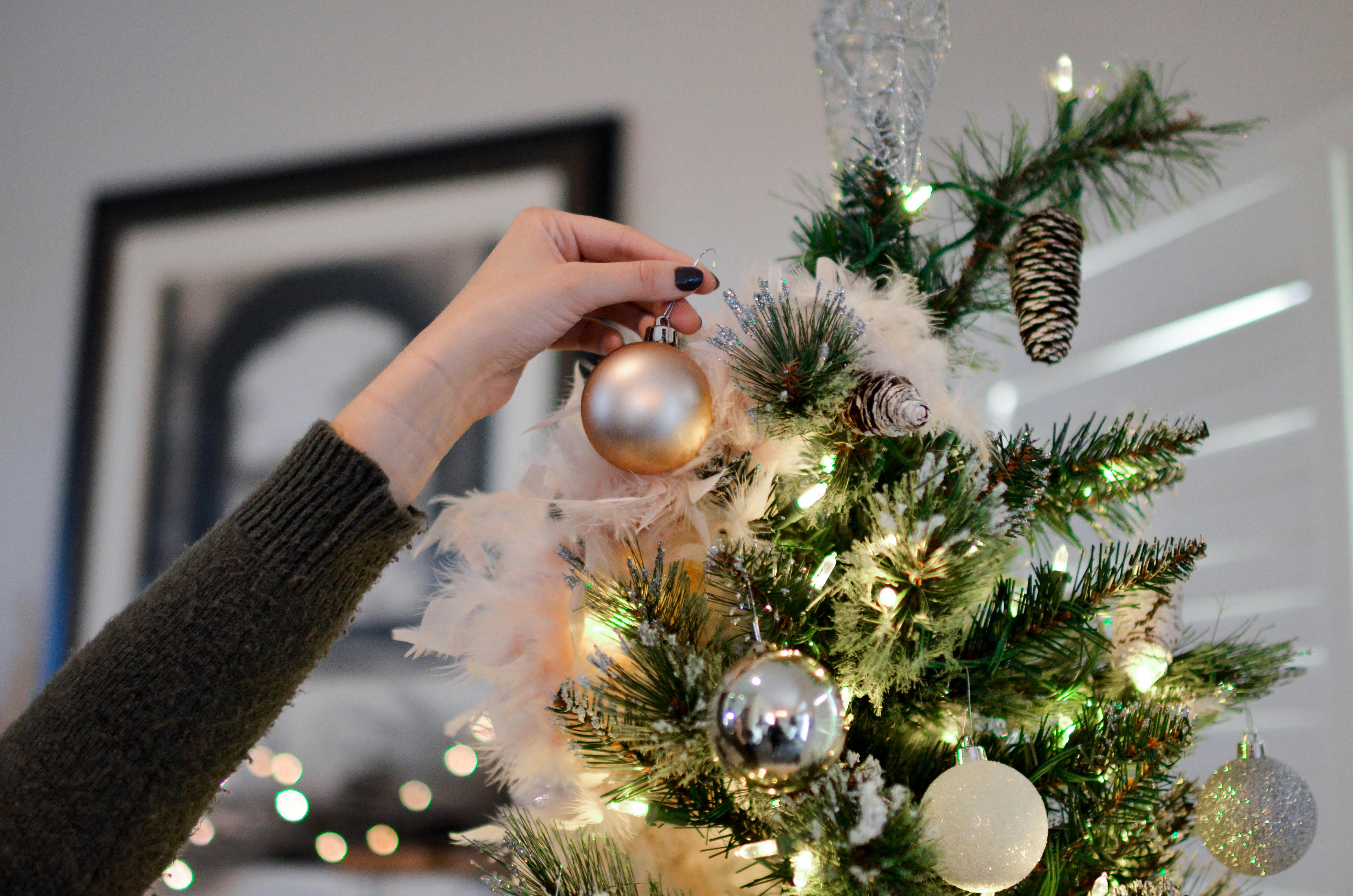 Comment décorer sa maison pour Noël - Une femme en train d’accrocher une boule dorée sur son sapin de Noël.