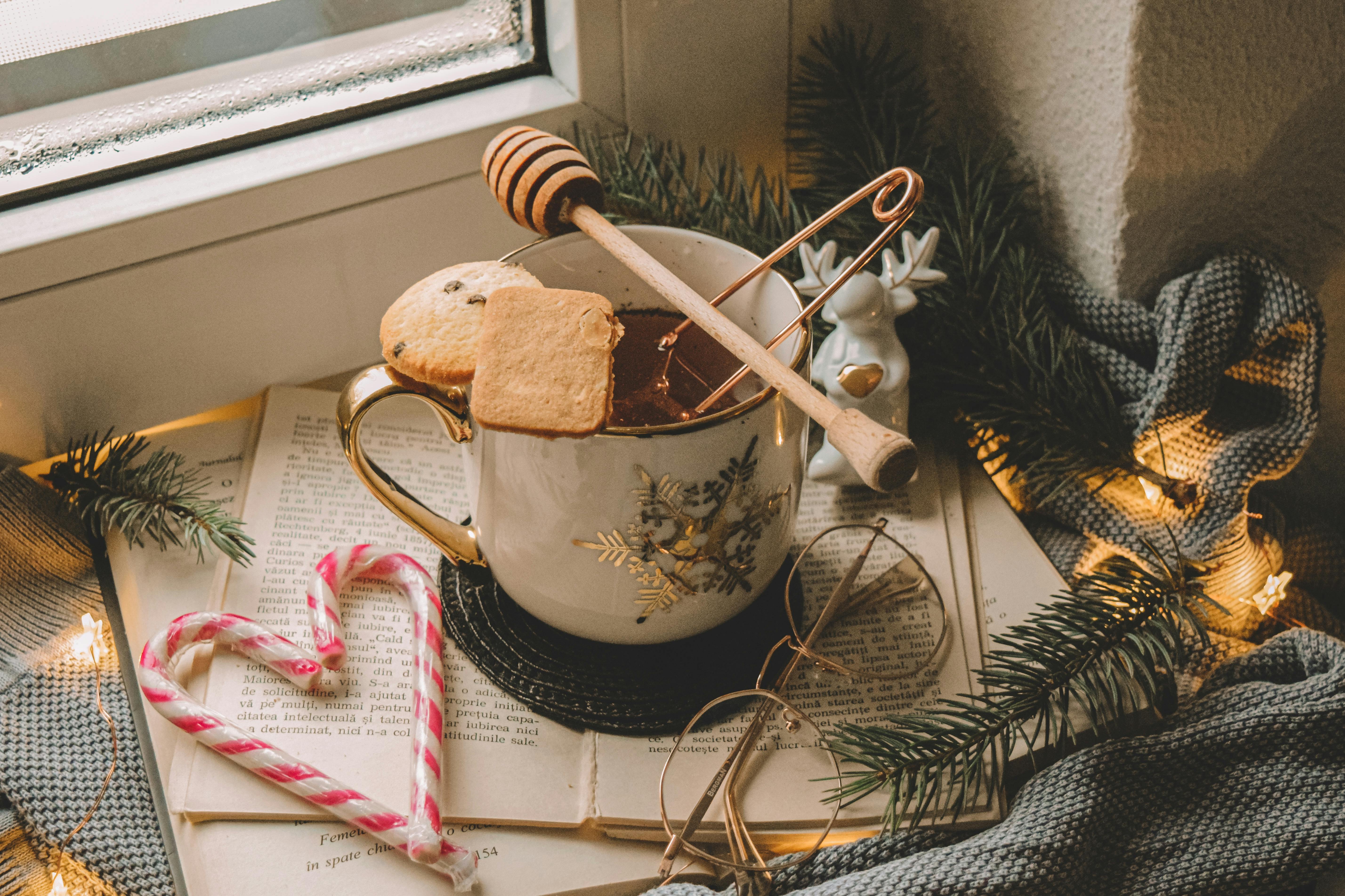 Comment décorer sa maison pour Noël - Une tasse thé posé sur le rebord d’une fenêtre qui est décoré sur le thème de Noël avec des branches de sapin et des à sucre.