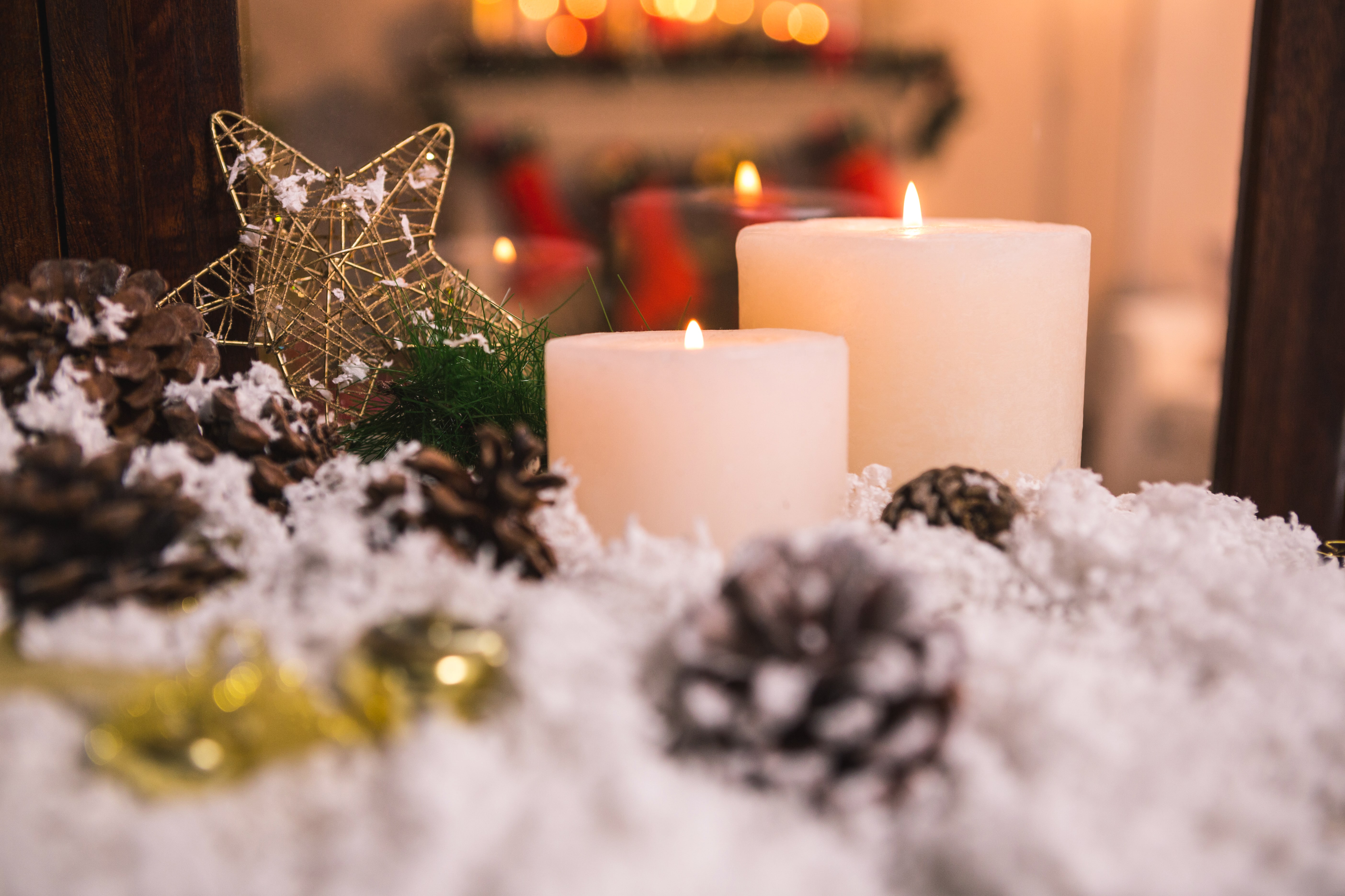 Comment décorer sa maison pour Noël - Des bougies parfumées allumées aux senteurs de Noël entourées de fausse neige et de pommes de pin.