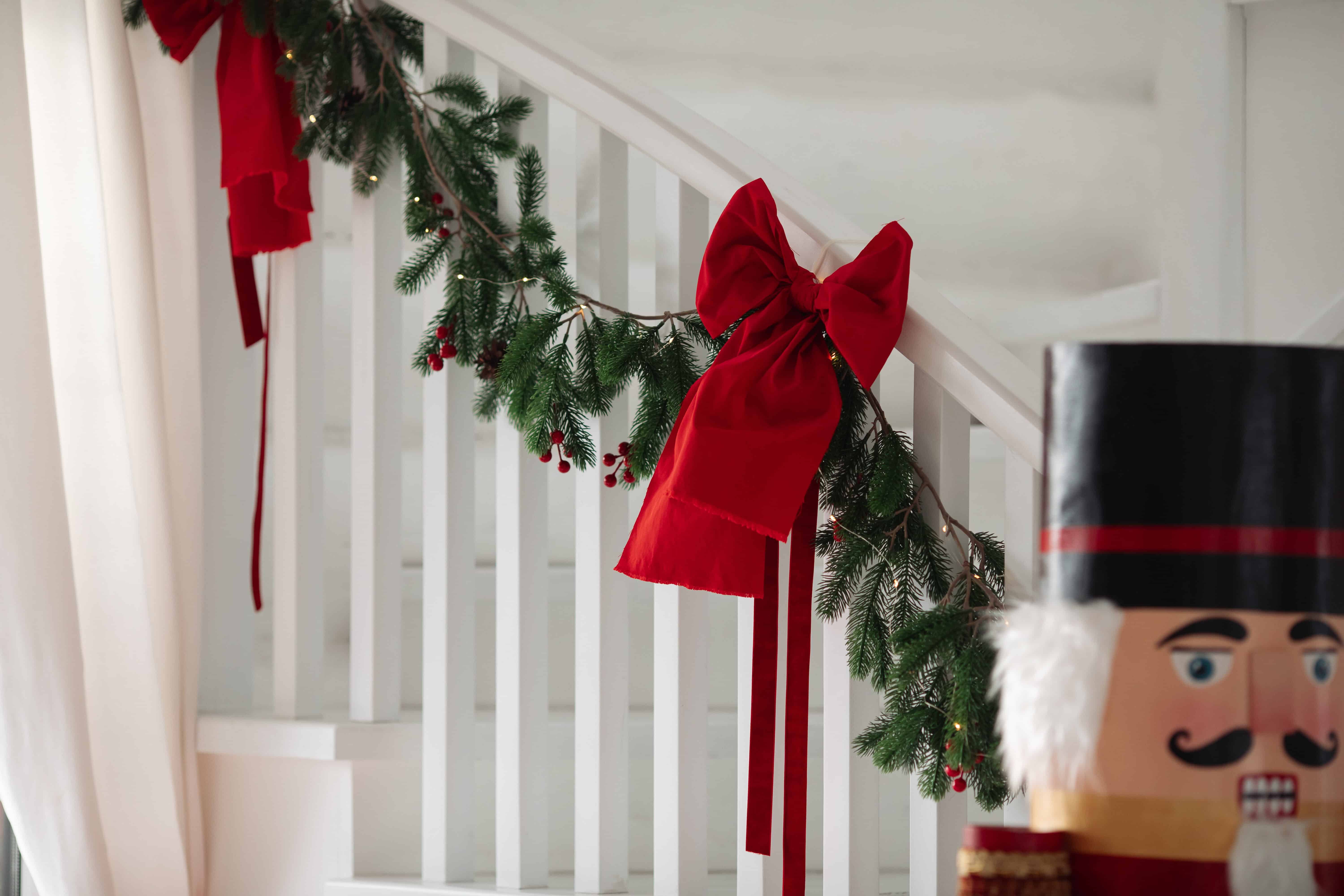 Comment décorer sa maison pour Noël - Une rampe d’escalier décorée avec du gui et des rubans rouges en forme de nœud.